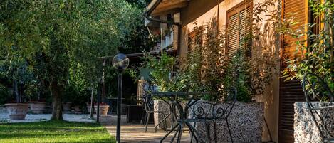 A courtyard with a stone pathway, outdoor seating, and a building with wooden shutters.