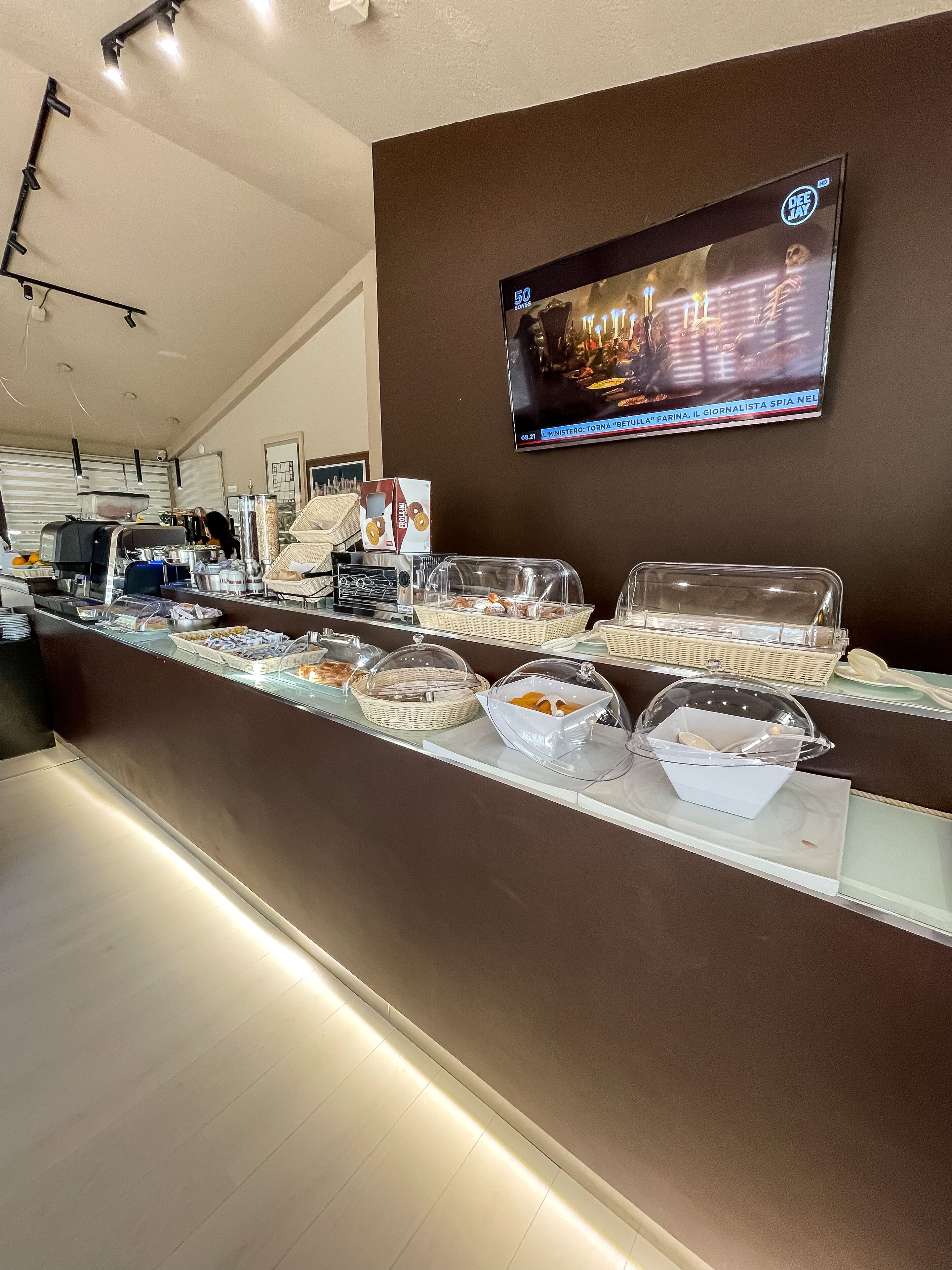 Uma área de buffet com diversos alimentos e uma televisão exibindo um noticiário.