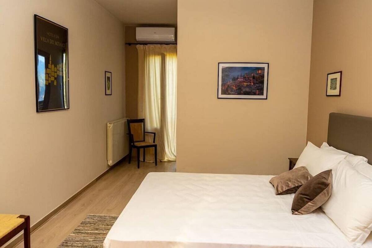 A hotel room with a bed, a chair, a radiator, and a poster on the wall.