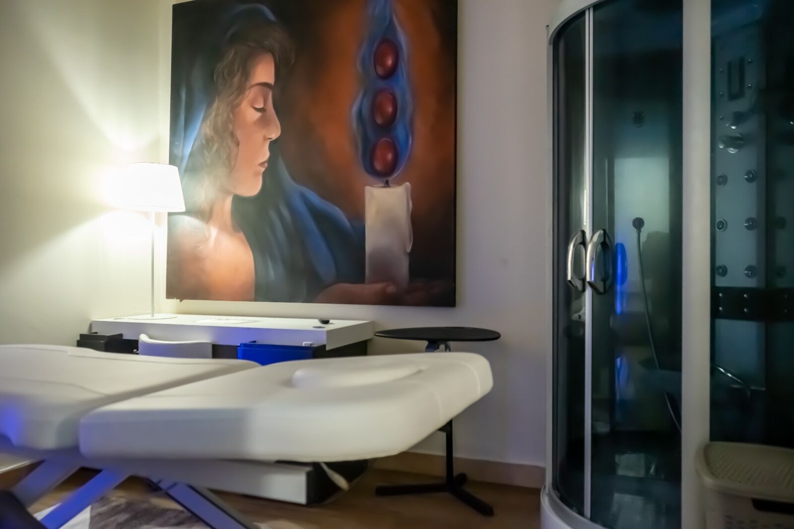 Una habitación con una mesa de masajes, un cuadro y un box de ducha de vidrio.