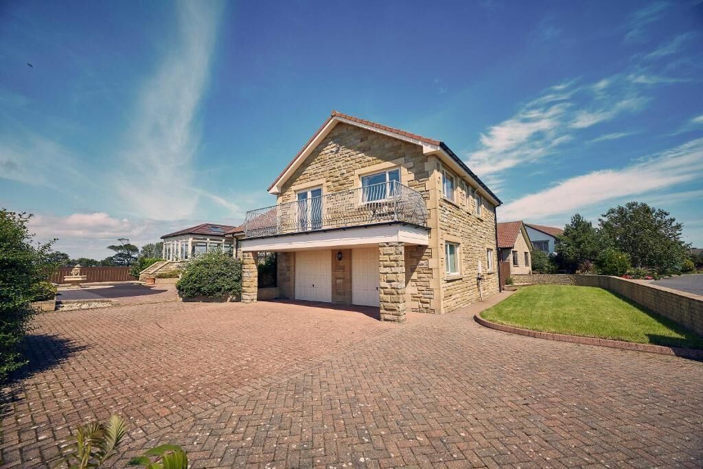 A two-story stone house with a garage, a covered driveway, and a well-maintained lawn.