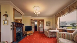 A living room with a fireplace, television, patterned sofa, and a large window with a view. - Host & Stay | Cheviot View (Seahouses)
