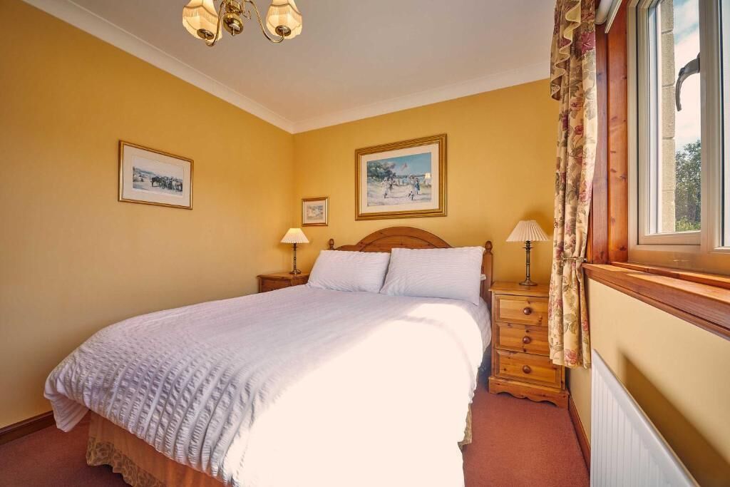 A bedroom with a bed, two bedside tables, a window with curtains, and two wall-mounted lamps.