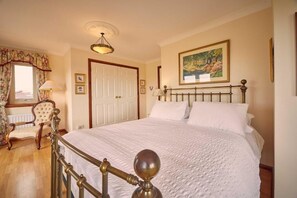 A bedroom with a bed, a chair, a door, a painting, and a lamp.