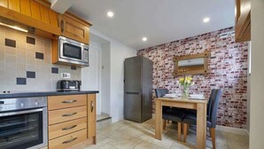Una cocina con armarios de madera, microondas, refrigerador y una mesa de comedor con sillas.