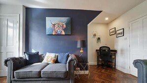 Una sala de estar moderna con un sofá gris, un cuadro de un toro y una lámpara de pie geométrica.
