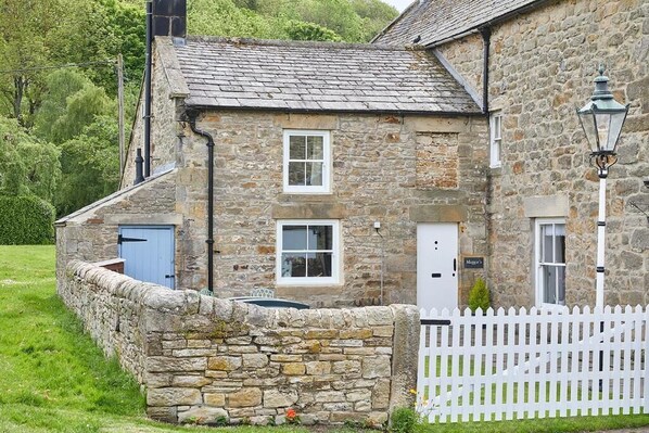 A stone building with a white picket fence, a small garden, and a sign that reads "Maggie's."