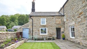 Une maison en pierre avec un petit jardin et une terrasse dallée.