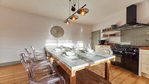 Une cuisine moderne avec une table à manger pour six personnes, une grande horloge au mur et un poêle noir.