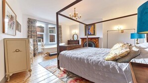 Un lit à baldaquin, une commode, un miroir, une cheminée et une fenêtre avec des rideaux.