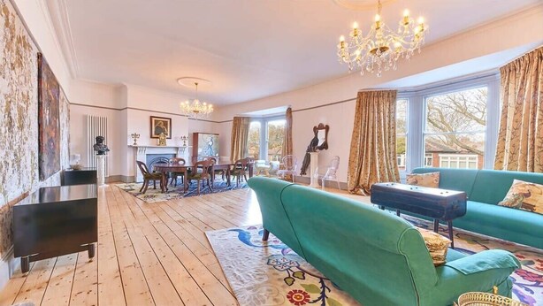Un salon spacieux avec un canapé vert, un parquet en bois, un lustre et une cheminée.
