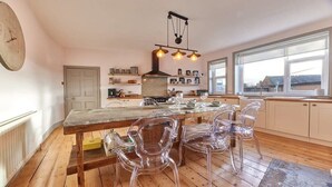 Une cuisine avec un plancher en bois, un îlot central doté de chaises, une cuisinière et un luminaire suspendu.