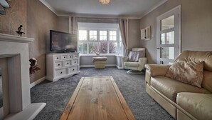 Una sala de estar con televisor, chimenea, sofá y ventana con cortinas.