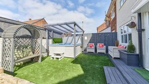 Patio trasero con jacuzzi, mobiliario exterior y una pérgola.
