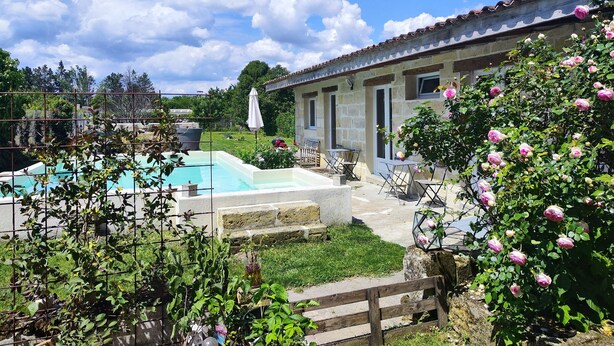 A pool area with a stone wall, outdoor seating, and a garden with blooming flowers. - cottage swimming pool 8km st emilion (sainte terre)