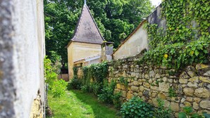 A narrow stone pathway leading to a small building with a tiled roof, surrounded by lush greenery and a stone wall. - cottage swimming pool 8km st emilion (sainte terre)