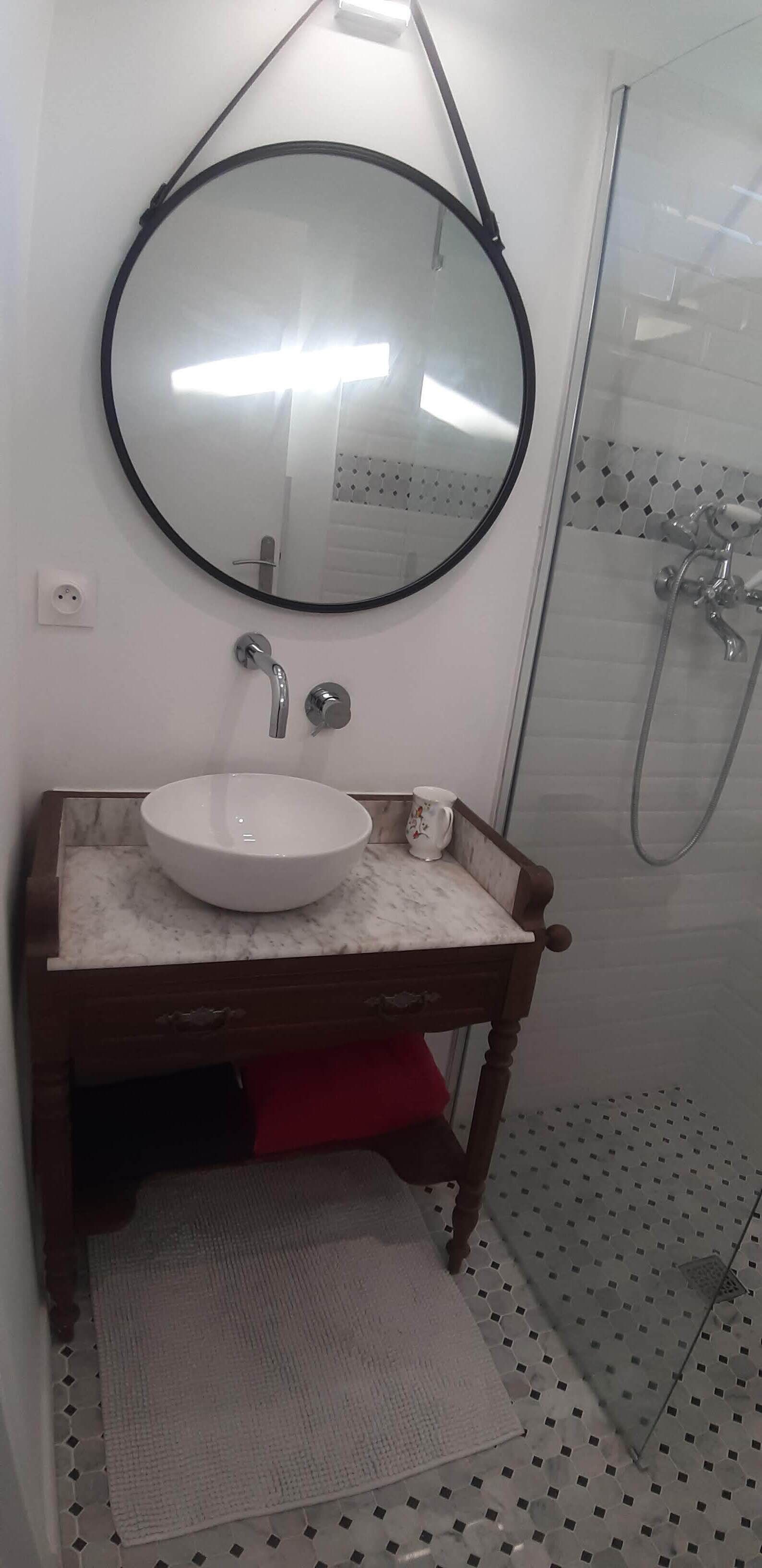 Une salle de bain avec un miroir rond, un lavabo et une douche.