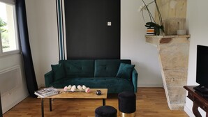 A living room with a dark green sofa, a wooden coffee table with books and flowers, black ottomans, and a stone fireplace. - cottage swimming pool 8km st emilion (sainte terre)