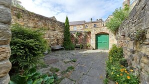 A stone courtyard with a green door, stone walls, and a bench.