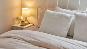 A neatly made bed with white bedding and pillows, a bedside lamp, and a small vase with flowers on a bedside table. - Host & Stay | The Burrow (Alnwick)