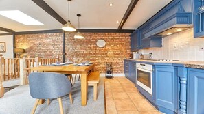 A kitchen with blue cabinets, a brick wall, and a dining area with a wooden table and chairs.