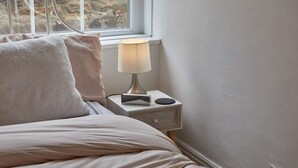 A bed with pillows, a bedside lamp, and a nightstand with a book and a remote control. - Host & Stay | The Burrow (Alnwick)