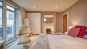 A bedroom with a large bed, a chair, a fireplace, and a view through a window. - Host & Stay | The View Old Coastguard Cottage (North Shields)