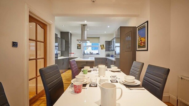 A dining area with a white table set for four, surrounded by black chairs. A kitchen is visible in the background. - Host & Stay | The View Old Coastguard Cottage (North Shields)