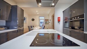 A modern kitchen with a central island, built-in appliances, and a dining area in the background. - Host & Stay | The View Old Coastguard Cottage (North Shields)