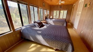 A room with two beds, large windows, a ceiling fan, and wooden walls. - Sweet Riverside Cabin, Easy Walk 2 River, Private River Access, River Views! (Concan)