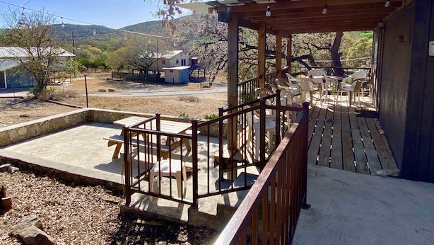 A covered outdoor patio with wooden railings, plastic chairs, and tables. - Sweet Riverside Cabin, Easy Walk 2 River, Private River Access, River Views! (Concan)