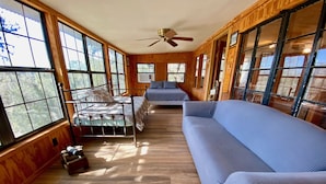 A cabin interior with a bed, a sofa, and a dining table. - Sweet Riverside Cabin, Easy Walk 2 River, Private River Access, River Views! (Concan)