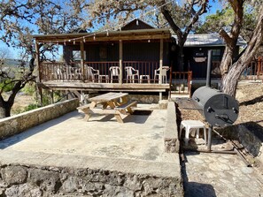 A wooden cabin with a porch, picnic table, barbecue grill, and outdoor seating.