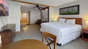 Ein Hotelzimmer mit Bett, Schreibtisch, Stuhl, Deckenventilator und einem Bild an der Wand.