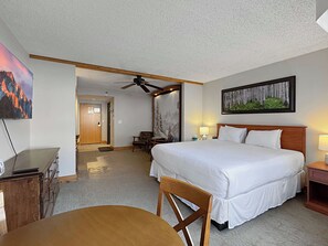 A hotel room with a bed, a desk, a chair, a ceiling fan, and a painting on the wall. - Grand Lodge #115   — Pet-Friendly Studio, Hot Tub, Pool, 5min to Red Lady Lift (Crested Butte)