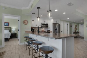 Une cuisine moderne dotée d’un îlot central, de tabourets de bar, d’appareils électroménagers en acier inoxydable et de luminaires suspendus.