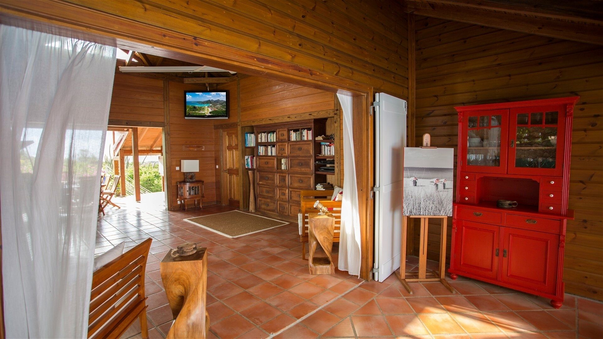 Ein Holzblockhaus-Interieur mit Fernseher, Bücherregalen, einem roten Schrank und einem Gemälde auf Staffelei.
