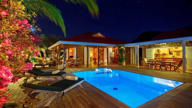 Un área junto a la piscina con sillones de descanso, una piscina y una cocina al aire libre techada.