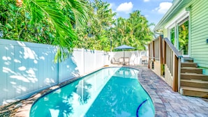 A swimming pool with a brick deck, surrounded by a white fence and lush greenery. - Anna Maria Home with Private Pool, Near the Beach! - Coveside Cottage (Holmes Beach)