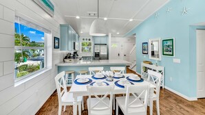 A modern kitchen with white cabinets, a stainless steel refrigerator, and a large island with a sink. - Anna Maria Home with Private Pool, Near the Beach! - Coveside Cottage (Holmes Beach)