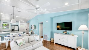 A modern living room with a white sofa, a coffee table, and a TV on a white cabinet. - Anna Maria Home with Private Pool, Near the Beach! - Coveside Cottage (Holmes Beach)