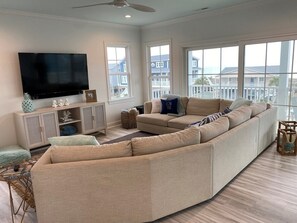 A living room with a large sectional sofa, a flat-screen TV, and a view of the outside.