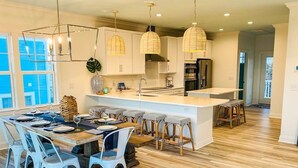 A modern kitchen with a central island, pendant lights, and a dining area with white chairs. - 1030 Ocean 5 Bedroom Home by RedAwning (Supply)