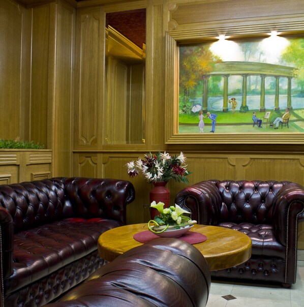 A room with two leather sofas, a wooden coffee table with a vase of flowers, and a large framed painting of a park scene on the wall.