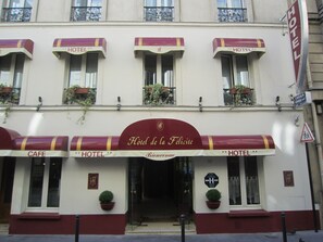 A building with multiple "HOTEL" signs and a "CAFE" sign. There are potted plants on the balconies and a pedestrian crossing sign.