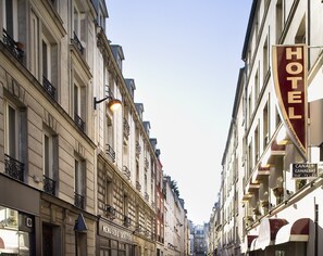 A hotel with a prominent 'HOTEL' sign, a 'CANAL+ CANAL SAT TNT- TV L.C.D' sign, and a 'MENUISERIE EBNESTERIE' sign.