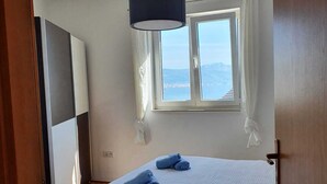 A bedroom with a bed, a window with curtains, a hanging light fixture, and a view of the mountains. - Romantic comfortable apartment (Trogir)