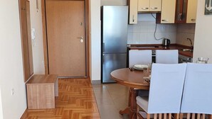 A compact kitchen with wooden cabinets, a built-in refrigerator, and a dining area with a table and chairs. - Romantic comfortable apartment (Trogir)