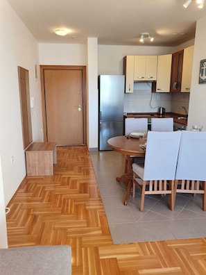 A compact kitchen with wooden cabinets, a built-in refrigerator, and a dining area with a table and chairs. - Romantic comfortable apartment (Trogir)