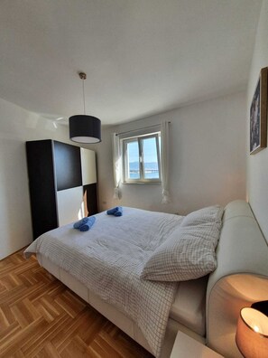 A bedroom with a bed, a bedside table, a lamp, a window with a view, and a wardrobe.